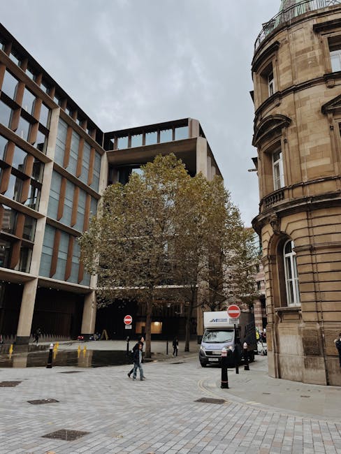 A view of a city street showing a modern multi-story office building with large glass windows and a concrete facade on the left, and an older, rounded stone building with detailed architectural featur